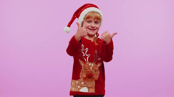 Vicces lány piros újévi pulóverben felemeli a hüvelykujját, egyetért valami jó dologgal, mint az ibolya háttér. - Fotó, kép