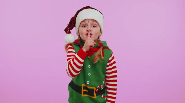 Child girl in Christmas Elf costume presses index finger to lips makes silence gesture sign, secret - Photo, Image