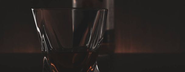 Banner with a glass of whiskey in the dark. Close-up glass of alcohol. Soft focus. - Foto, immagini