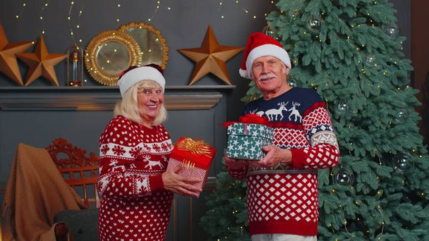 Romantikus idős pár ajándékdobozokat mutat be egymásnak otthon, a karácsonyfa díszítésének közelében - Fotó, kép