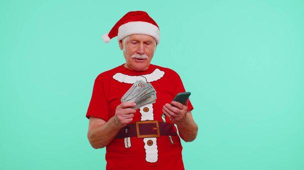 Noël grand-père regardant smartphone se réjouissant sincèrement gagner de la chance de succès en recevant de l'argent en ligne - Photo, image