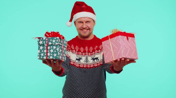 Mężczyzna nosi czerwony Nowy Rok prezentując pudełka świąteczne, wyciąga ręce do aparatu uśmiechając - Zdjęcie, obraz