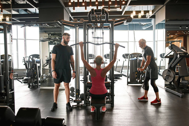 Personal trainer watching middle-aged woman weight lifting - Foto, afbeelding