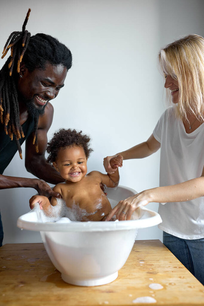 Mother and father washing little daughter in bathtube, child have fun, smiling - Photo, Image