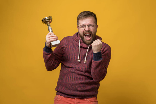 Victory. Happy man holds a gilded cup in hand and shouts with joy, he won a sports tournament and received the long-awaited award.  - Фото, изображение