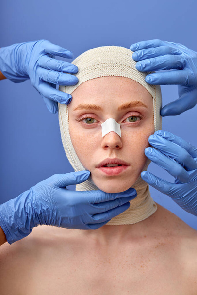 cropped surgeon in gloves taping up woman face with bandage after plastic surgery - Foto, Bild