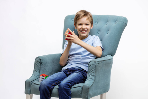 Kyiv, Ukraine, October 9 2021: Young boy solving mental puzzles. Child playing with pyramid puzzle and Rubik's cube while sitting in cozy armchair. - Photo, image