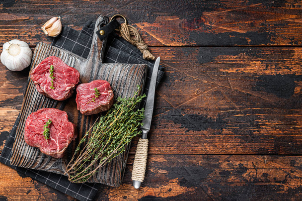 Prvotřídní syrové steaky Fillet mignon na dřevěné desce s tymiánem a česnekem. Tmavé dřevěné pozadí. Horní pohled. Kopírovat prostor - Fotografie, Obrázek
