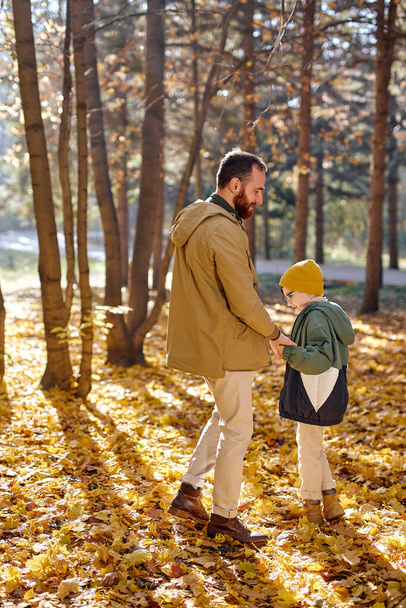 Бородатий чоловік батько ходить з сином хлопчиком в осінньому парку, лісі. сімейна концепція
 - Фото, зображення