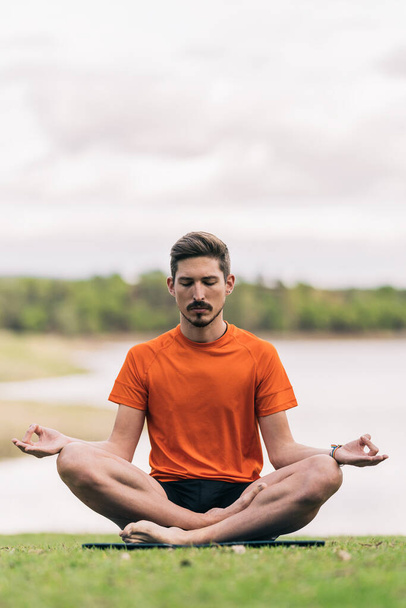 Homem com uma pulseira de arco-íris fazendo a posição de lótus de ioga ao ar livre - Foto, Imagem