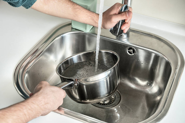 Man's hands filling a stainless steel saucepan with running water until it boils and cooks something. - Foto, Imagem
