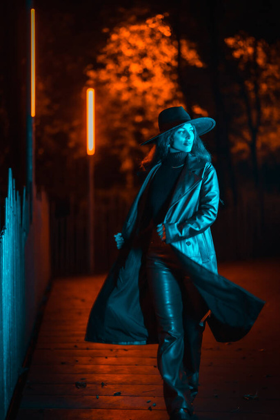 Caucasian brunette girl with hat at night in a park illuminated with blue light. Winter fashion and lifestyle at night - Valokuva, kuva