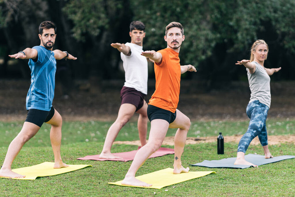 Personas levantando brazos mientras hacen una pose de yoga en un parque público - Foto, imagen