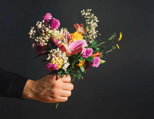 Vintage flower composition made of various autumn flowers and man's hand. Nature concept. Floral Greeting card for Valentines Day or 8 March. Black background. - Photo, Image