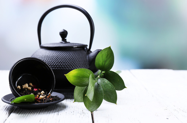 Tetera negra, tazón y té en la mesa de madera de color, sobre fondo brillante
  - Foto, Imagen