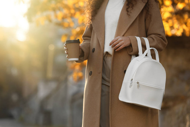 Young woman with stylish white backpack and hot drink outdoors on sunny day, closeup - Photo, Image