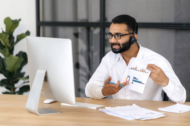 Online business video meeting. Irritated Indian entrepreneur or business mentor, talks via video call with partners, discusses a project, analyzes a business plan, shows a graph to his interlocutors - Photo, Image