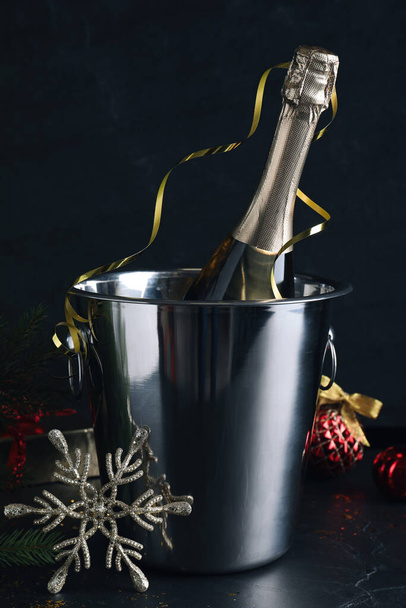 Happy New Year! Bottle of sparkling wine in bucket and festive decor on black background - Photo, image