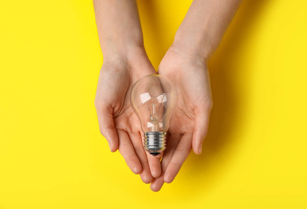 Woman holding light bulb on yellow background, top view - Zdjęcie, obraz