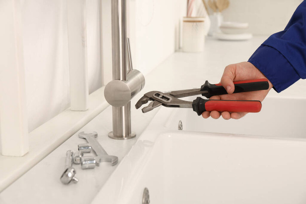 Plumber with spanner near sink in kitchen, closeup. Water tap installation - Фото, зображення