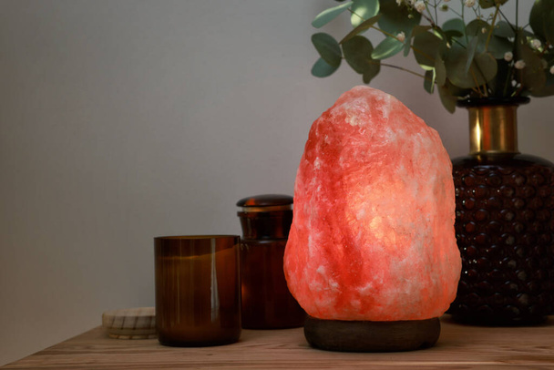 Beautiful Himalayan salt lamp, eucalyptus branches and candles on wooden table indoors, space for text - Фото, изображение
