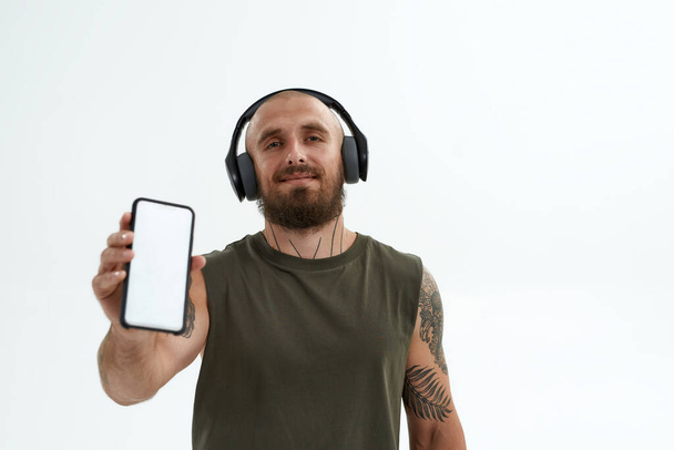 Man in headphones showing smartphone at camera - Foto, Imagen
