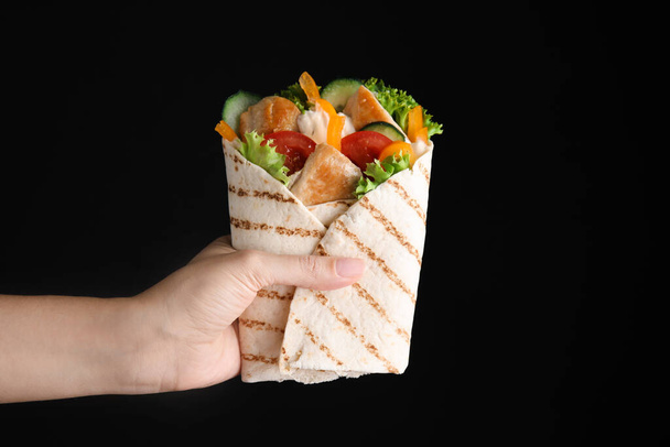 Woman holding delicious shawarmas with chicken meat and vegetables on black background, closeup - Valokuva, kuva