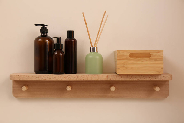 Wooden shelf with soap dispensers and aromatic reed freshener on beige wall. Interior element - Foto, imagen
