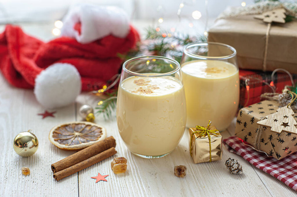 Two glasses of eggnog on a white wooden table next to the Christmas presents. Sweet egg dessert. Christmas breakfast. Selective focus - Foto, afbeelding
