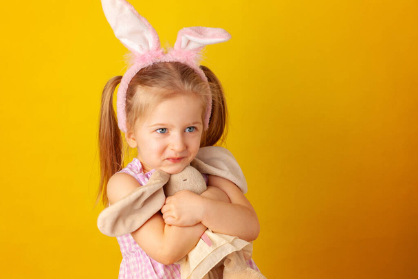 Little girl holding her bunny toy against yellow background - Foto, Bild