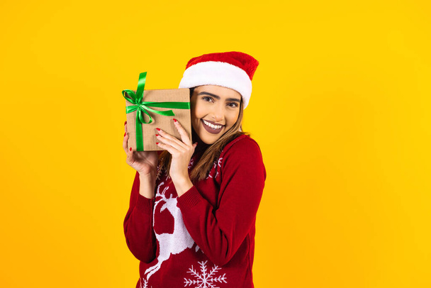joven latina sosteniendo regalos de Navidad en sombrero de Navidad sobre fondo amarillo en México América Latina - Foto, imagen