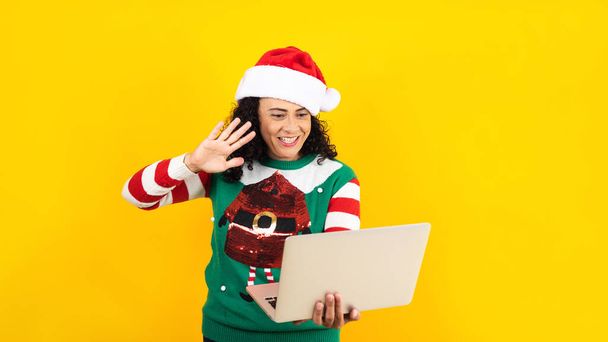 adult latin woman having christmas video call using digital tablet or touchpad on a yellow background - Photo, Image