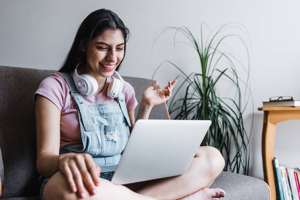 junge Lateinschülerin mit Kopfhörer mit Laptop in einem Videoanruf oder Online-Kurs, während sie zu Hause auf dem Sofa sitzt  - Foto, Bild