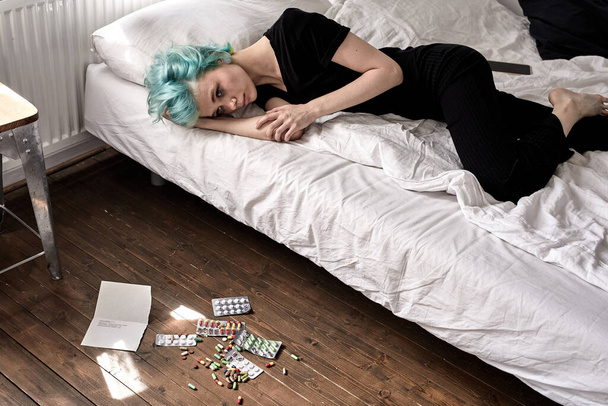 Suicide by medication overdose concept. pills on floor and young woman with depression - Foto, Imagem