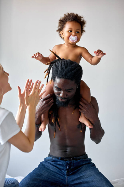 Funny black child girl sitting on neck shoulders of father, having fun, at home - Foto, Imagem