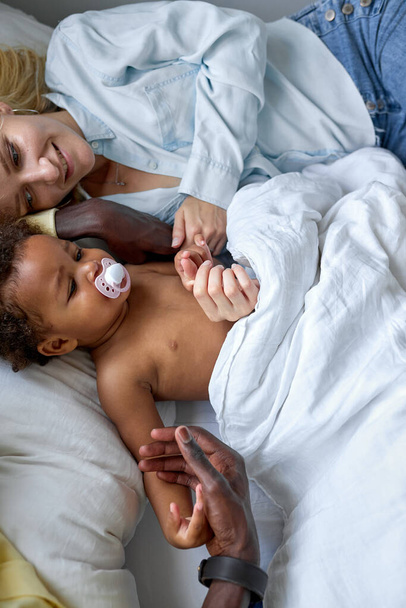 Interracial family with child girl spend weekends morning on bed at home, love concept - Foto, imagen