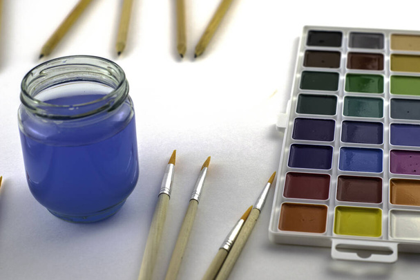 akvarell festékek ecset egy üveg víz és ceruzák egy fehér háttér másolás. Kiváló minőségű fénykép - Fotó, kép
