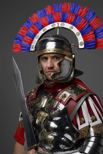 Pyšný římský voják s gladius pózování proti šedému pozadí - Fotografie, Obrázek