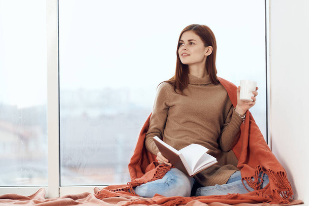 woman with a cup of drink on the windowsill reading a book rest morning - Foto, imagen