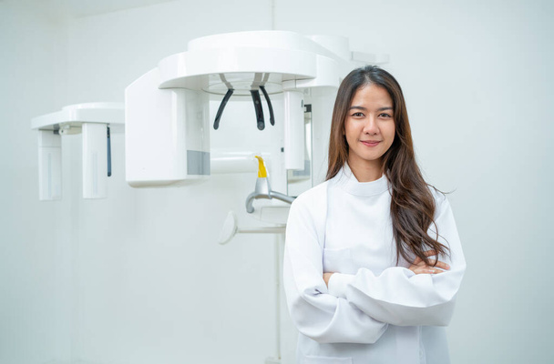 Bella asiatica dentista donna stand con braccio incrociato o fiducioso di fronte alla macchina a raggi X dentale. - Foto, immagini