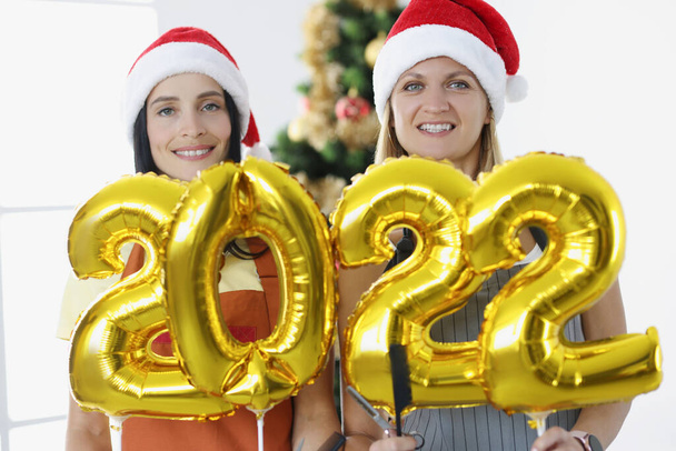 Две улыбающиеся женщины-стилиста держат номера 2022 на фоне новогодней елки. - Фото, изображение