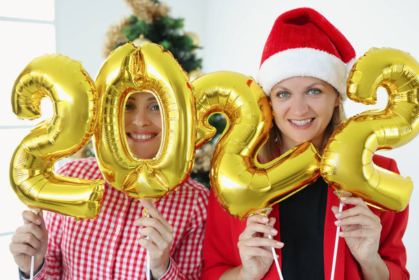 Two smiling women hold numbers 2022 against background of New Year tree - Foto, immagini