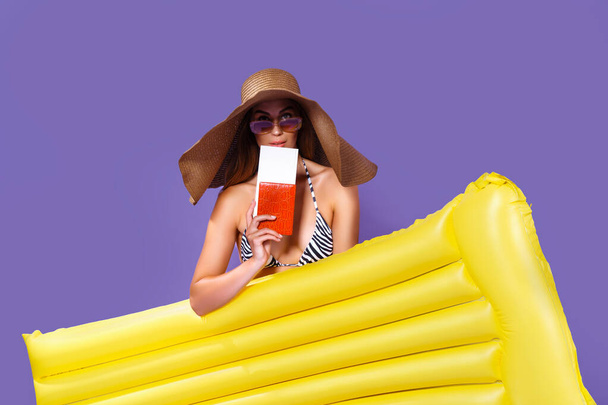 Beauty girl in sunhat going to travel stands with yellow inflatable mattress shows ticket, passport - Fotografie, Obrázek