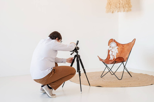 Minimaal licht en luchtig interieur. Man fotograaf werkt in een minimaal licht en luchtig interieur, wit en beige stoel, tapijt en kussens - Foto, afbeelding