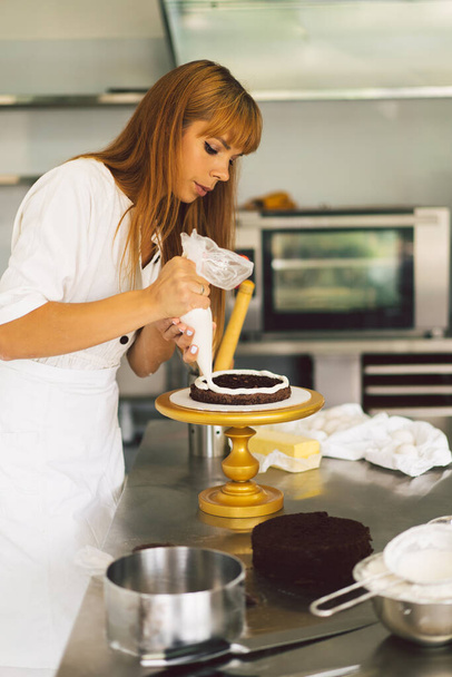 Cukierniczka przygotowuje ciastko z białą śmietaną i czekoladą. Ciasta kuchenne. - Zdjęcie, obraz