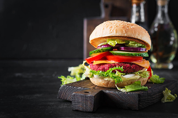 Gesunde vegane Rote-Bete-Burger mit Tomate, Gurke, roter Zwiebel und Sauce. Dunkler Hintergrund. Kopierraum. - Foto, Bild