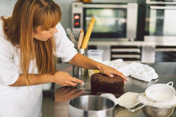 Confectioner girl is preparing a cake biscuit with white cream and chocolate. Cooking cakes. - Photo, Image