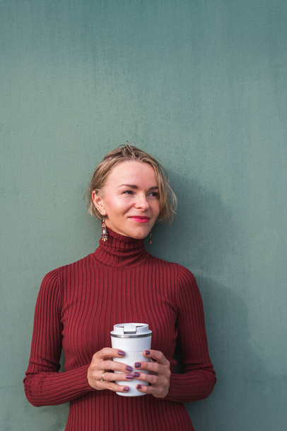 szőke nő tart szünetet közel a zöld fal és a kezében egy elviszi kávé - Fotó, kép