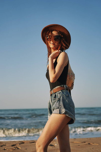 cheerful woman in a hat with sunglasses walking with a bag - Foto, imagen