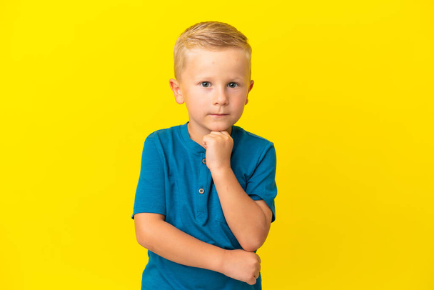 Μικρό ρωσικό αγόρι απομονωμένο σε κίτρινο φόντο έχοντας αμφιβολίες και σκέψη - Φωτογραφία, εικόνα